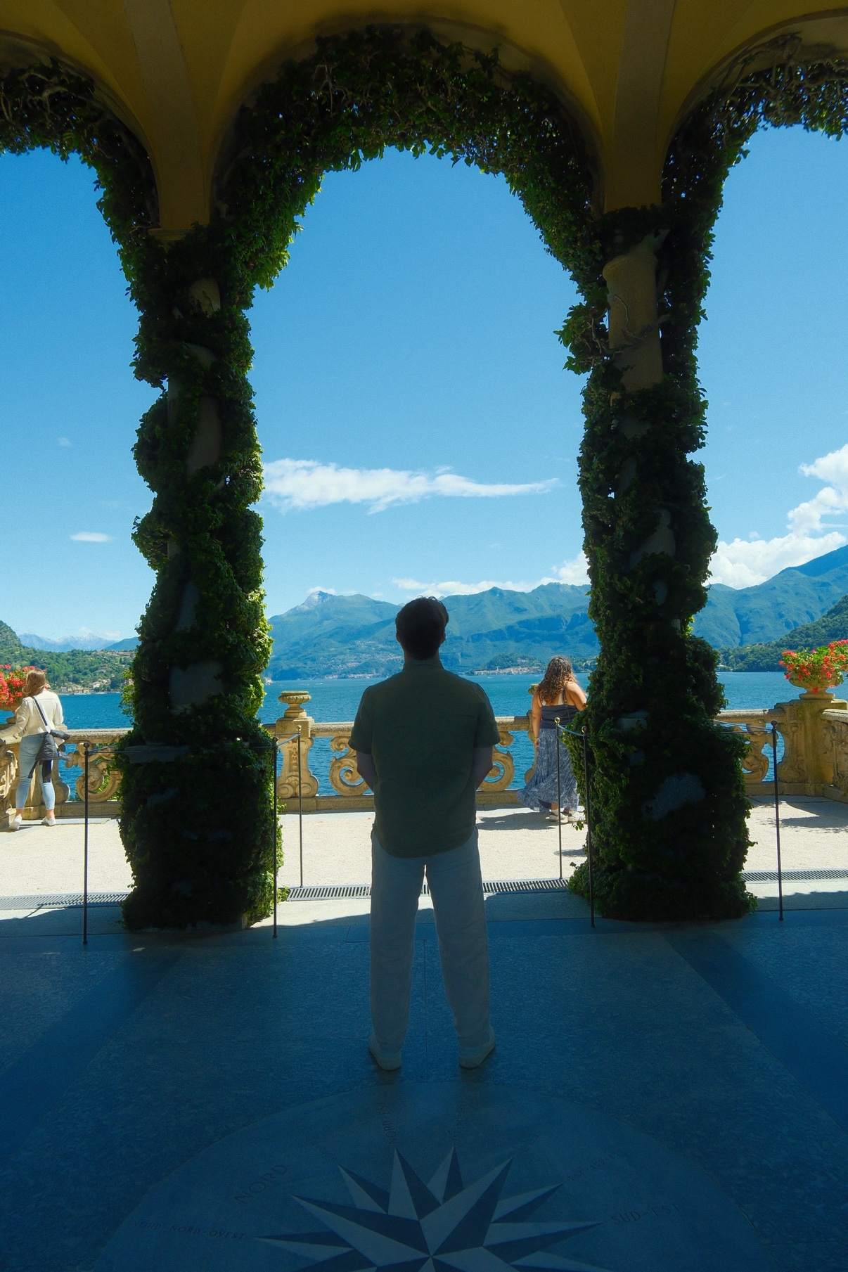 Brendan's silhouette framed by an ivy-covered stone arch overlooking Lake Como at Villa del Balbianello
