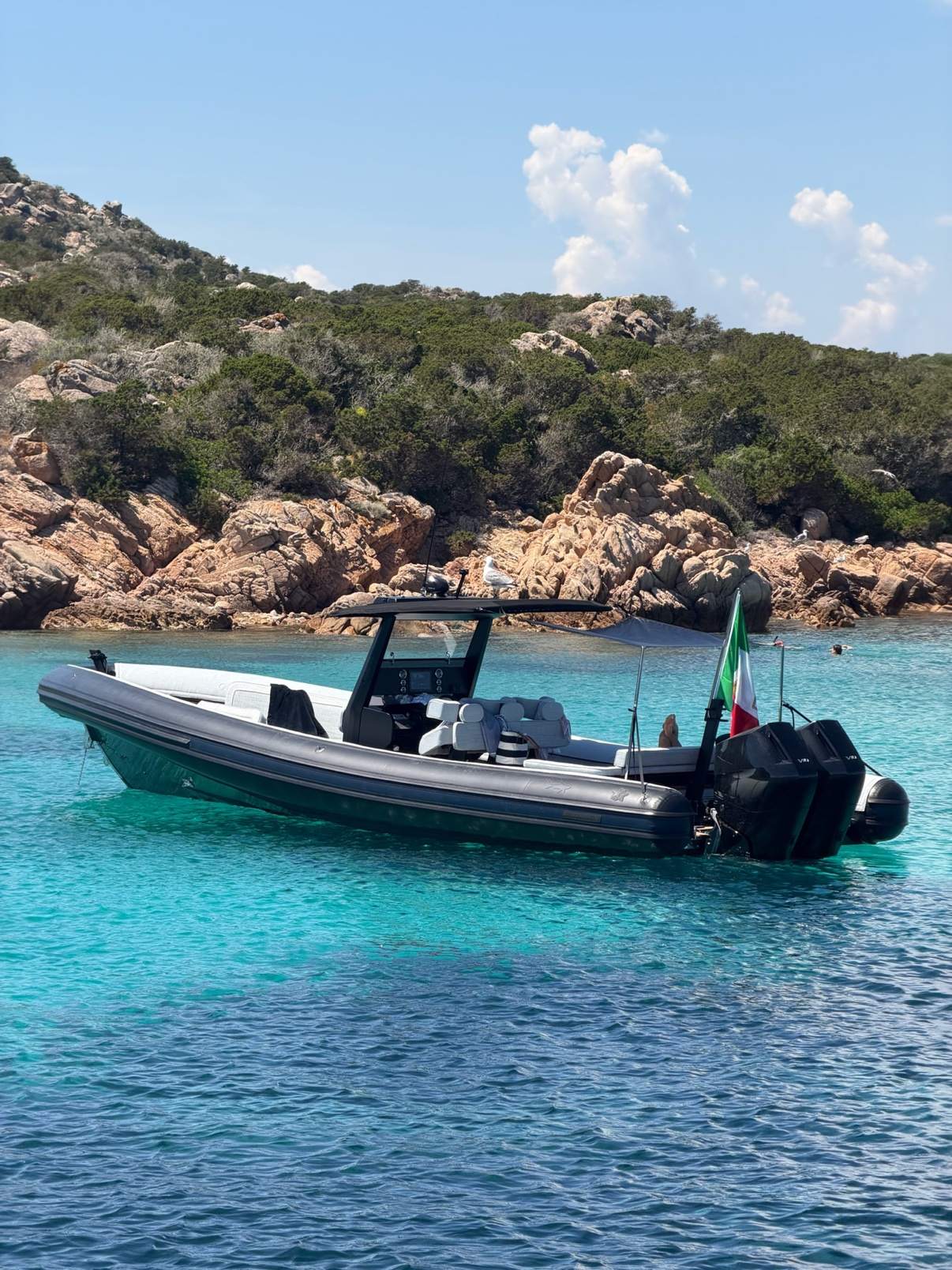 A rigid inflatable boat flying an Italian flag anchored in turquoise water off Sardinia