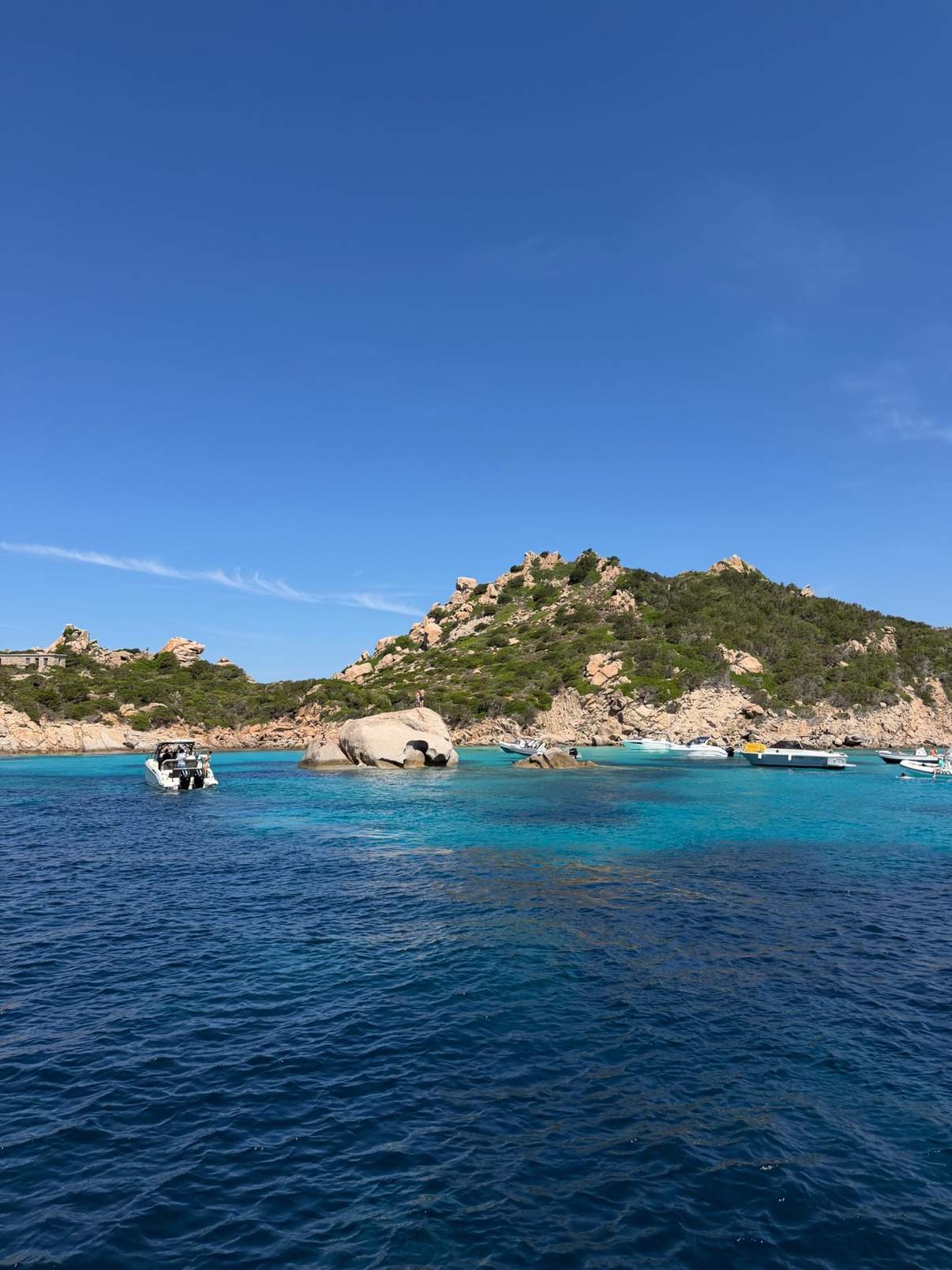 Turquoise water and granite islets in a Sardinian cove with boats at anchor