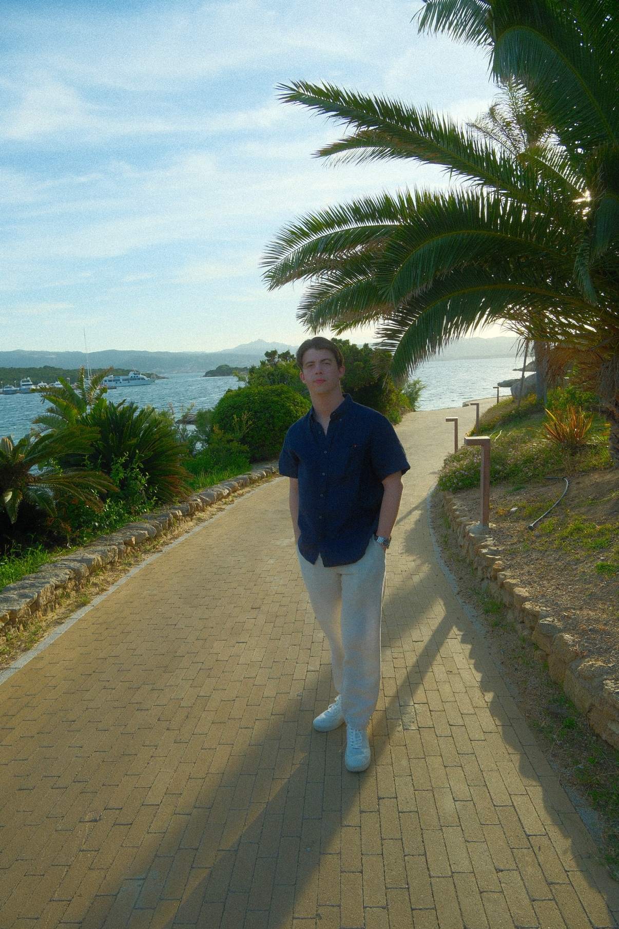 Brendan on a palm-lined brick path by the water in Sardinia at golden hour